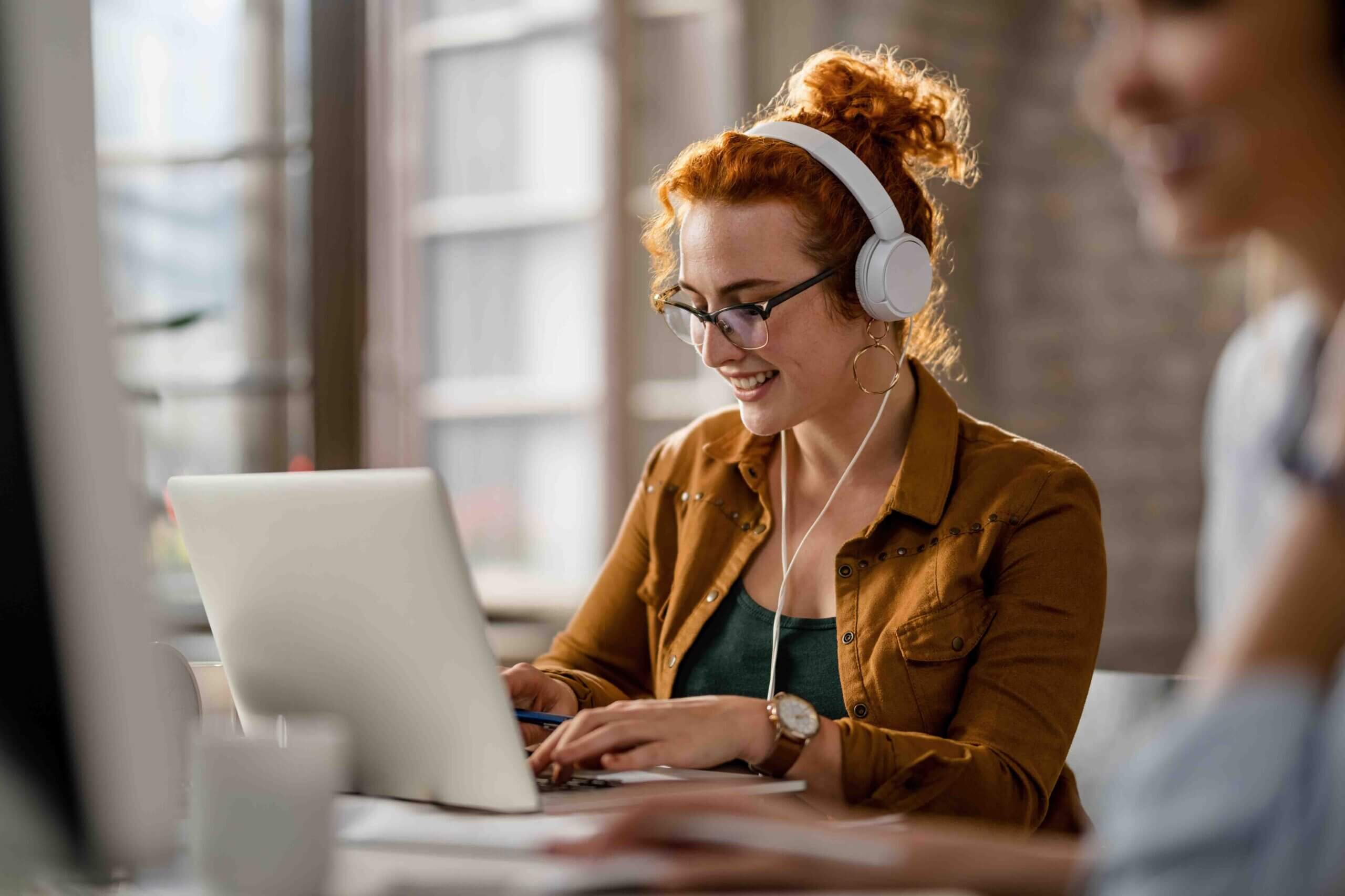 smiling-creative-businesswoman-listening-music-headphones-while-working-computer-office